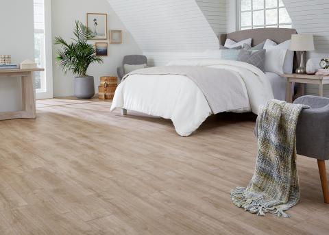 This bedroom uses neutral colors, soft textiles, and rigid vinyl plank flooring.